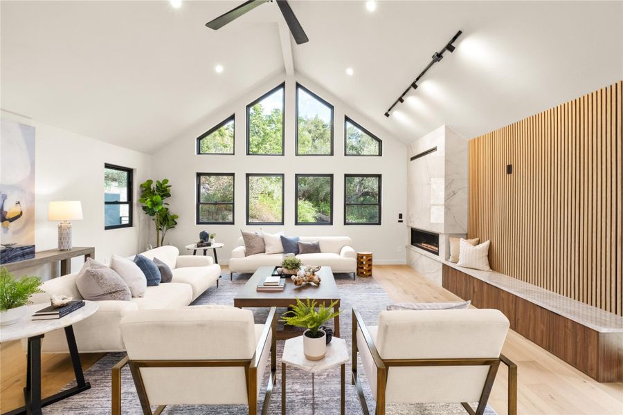 Living room featuring light wood-type flooring, a ceiling fan, a fireplace, and high vaulted ceiling