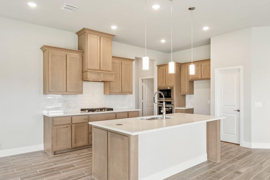 Kitchen with light wood cabinets, large center island, pendant lights, and stainless steel appliances