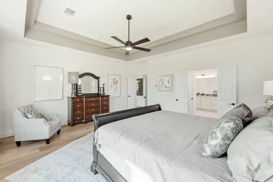 Master bedroom with tray ceiling, ceiling fan, hardwood floors, and dark wood dresser with mirror