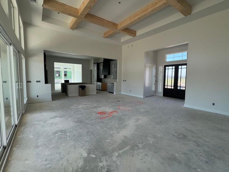 Unfurnished bedroom with beamed ceiling, coffered ceiling, french doors, a towering ceiling, and unfinished concrete flooring