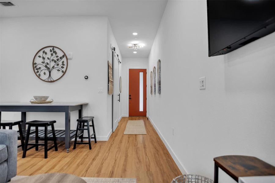 Hallway featuring baseboards, a barn door, visible vents, and wood finished floors