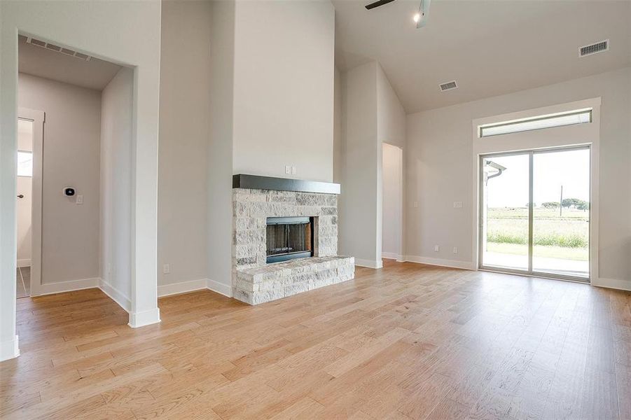 Unfurnished living room with a stone fireplace, light hardwood / wood-style flooring, and ceiling fan