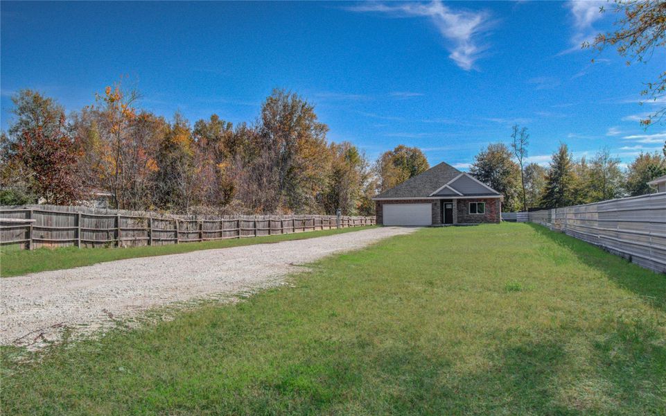 Charming home with a long gravel driveway, surrounded by greenery and mature trees. The property is fenced on both sides, offering privacy and a spacious lawn area.