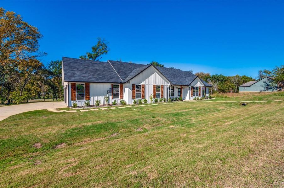 Modern farmhouse style home featuring roof with shingles, a front yard, and a porch