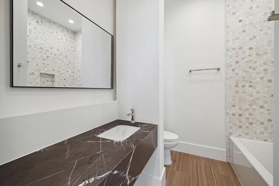 The guest suite bathroom boasts a tub/shower combo with marble hexagon tile walls, complemented by a Signature Hardware soaking tub and Miseno plumbing fixtures. Marble countertops and stone tile flooring elevate the space's elegance, while a floating vanity with white painted storage cabinetry offers both style and functionality.