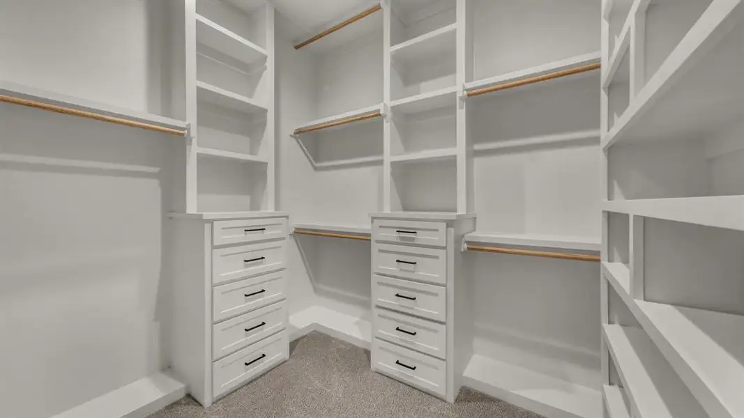 Spacious custom closet featuring extensive white built-in shelving, multiple hanging rods, two built-in drawer units with matte black hardware, and soft gray carpeting Spacious custom closet featuring extensive white built-in shelving, multiple hanging rods, two built-in drawer units with matte black hardware, and soft gray carpeting