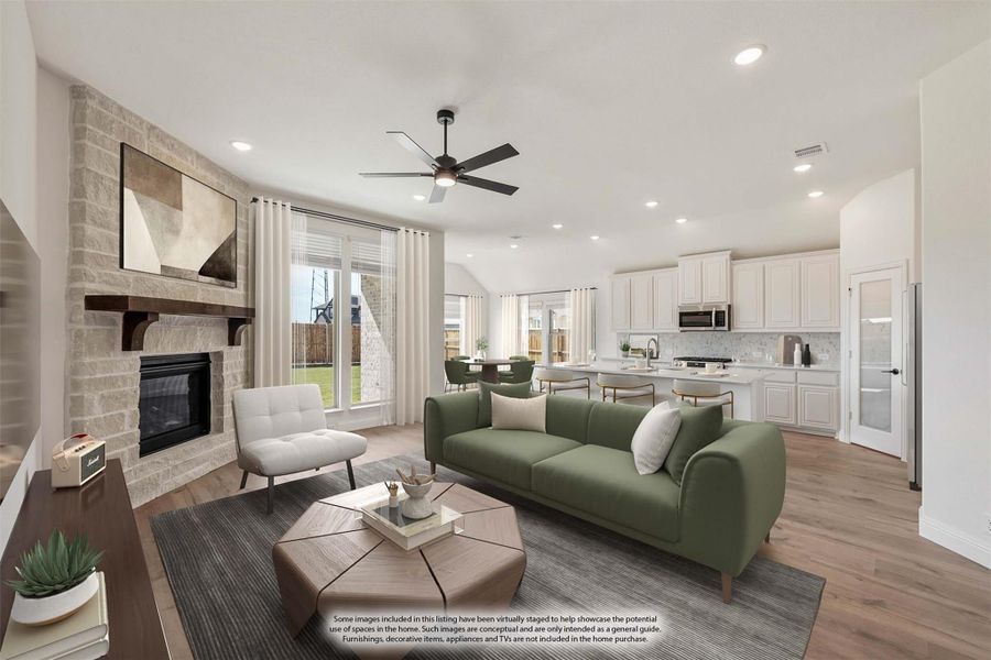 Open living room with stone fireplace, ceiling fan, and green sofa flowing into kitchen with white cabinets Open living room with stone fireplace, ceiling fan, and green sofa flowing into kitchen with white cabinets