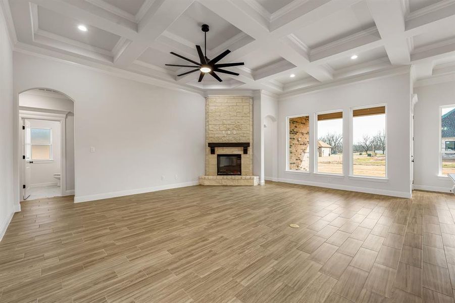 Unfurnished living room featuring ceiling fan, crown molding, a stone fireplace, and beamed ceiling