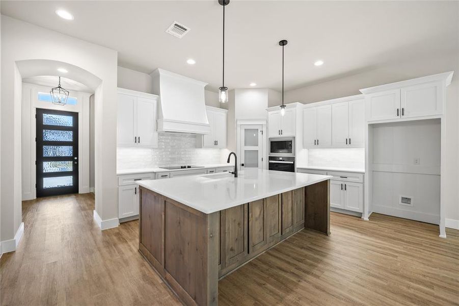 Kitchen with white cabinets, tasteful backsplash, a kitchen island with sink, and recessed lighting