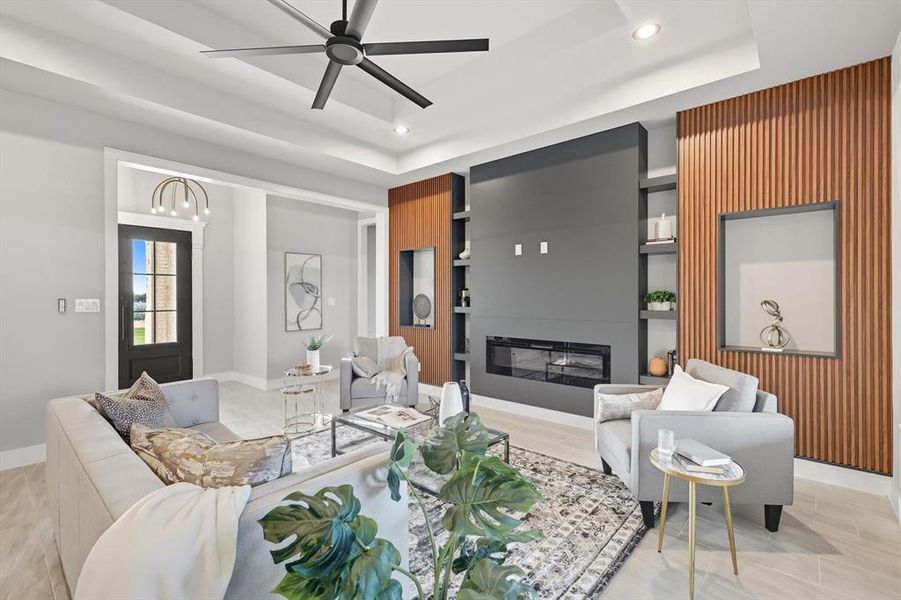 Living area featuring built in features, a glass covered fireplace, ceiling fan, a tray ceiling, and recessed lighting Living area featuring built in features, a glass covered fireplace, ceiling fan, a tray ceiling, and recessed lighting