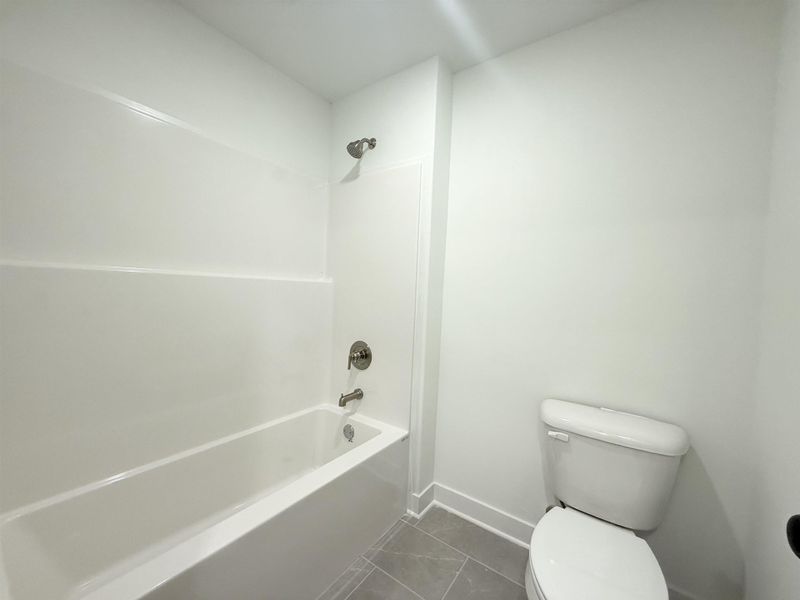 Bathroom featuring tub / shower combination and dark tile patterned floors