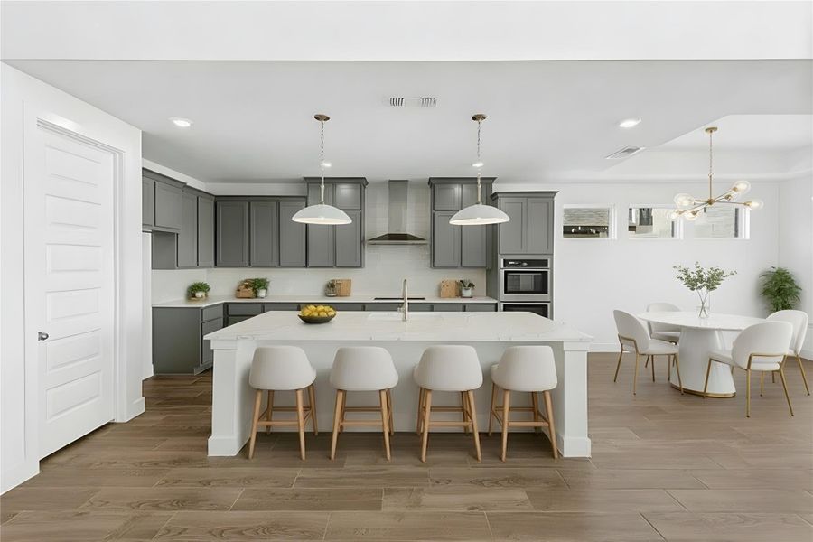 Kitchen featuring gray cabinetry, a breakfast bar area, hanging light fixtures, wall chimney range hood, and light wood-style floors