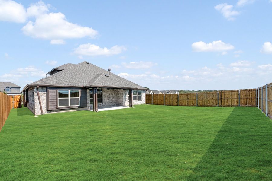 Rear view of brick home with large fenced backyard, covered patio, and green lawn Rear view of brick home with large fenced backyard, covered patio, and green lawn