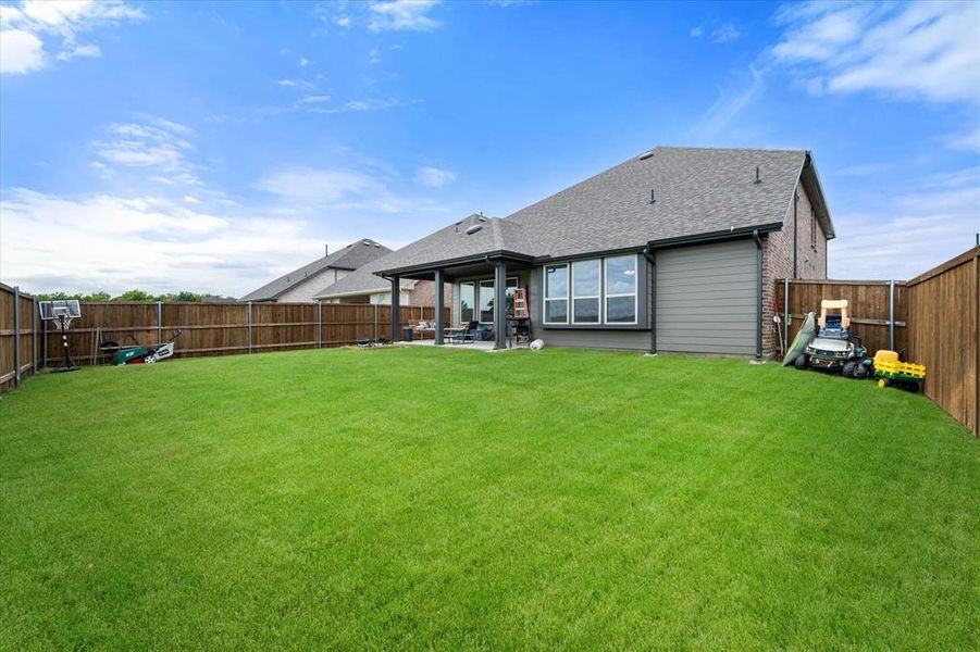 Expansive backyard featuring a lush lawn, privacy fencing, and a covered patio area