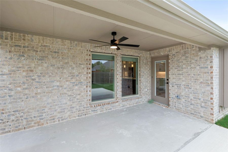 Covered back patio with ceiling fan, brick exterior wall, large window, and back door leading inside. Covered back patio with ceiling fan, brick exterior wall, large window, and back door leading inside.