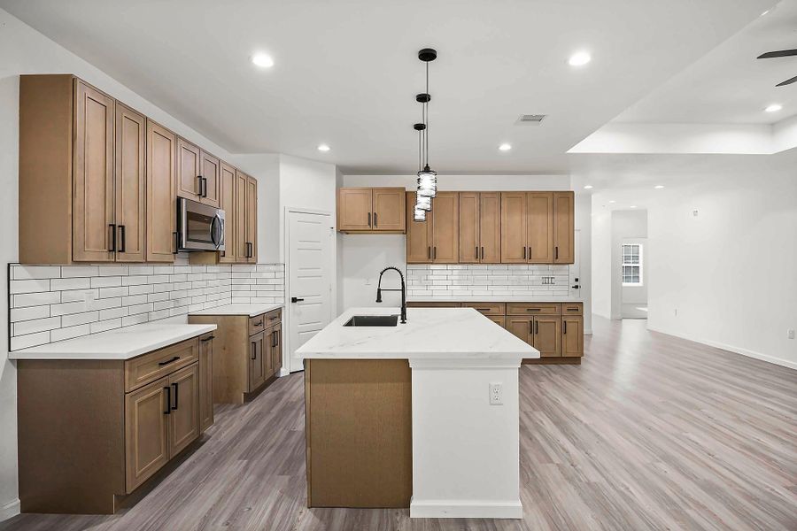 Spacious modern kitchen featuring sleek wood cabinetry, a large island with a sink, and elegant pendant lighting, complemented by a subway tile backsplash and stainless steel appliances.