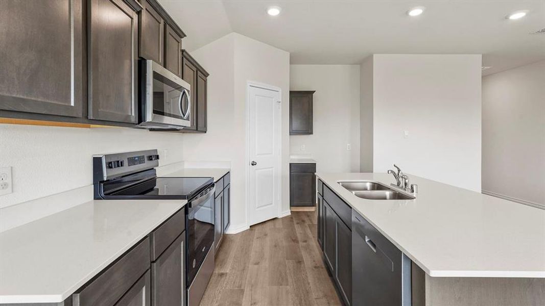 Modern kitchen featuring white countertops, dark wood-finish cabinetry, stainless steel appliances, and wood-finish flooring