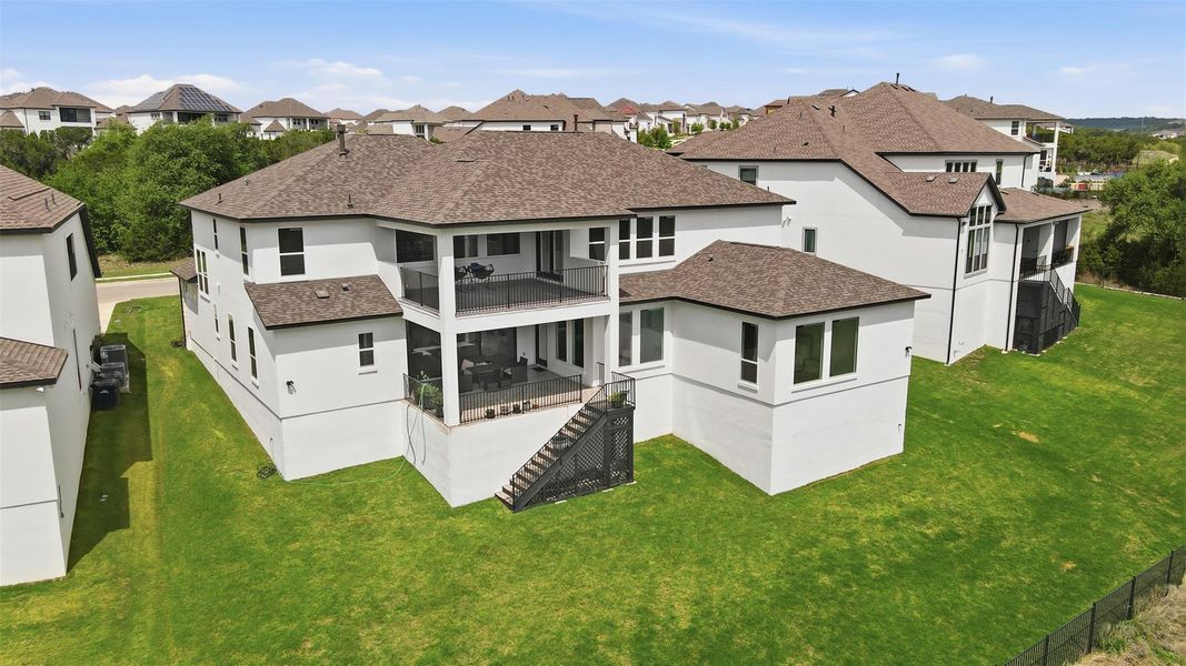 The property features a tiered backyard with extensive green lawn space and a dark metal fence