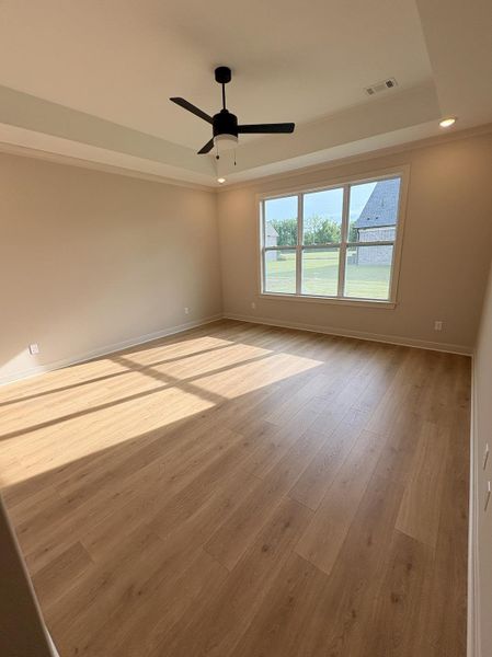 Spacious room featuring wood-finish flooring, a tray ceiling, and a ceiling fan with integrated lighting