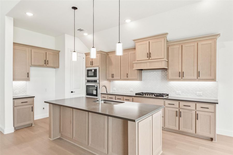 Kitchen with light wood cabinets, dark countertop island, pendant lights, and stainless steel appliances
