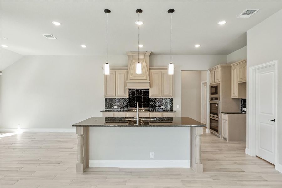 Kitchen with large island, dark granite countertops, cream cabinets, black tile backsplash, and pendant lights Kitchen with large island, dark granite countertops, cream cabinets, black tile backsplash, and pendant lights