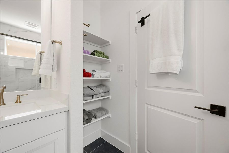 Open shelving in the primary bath combines style and function, offering attractive, easily accessible storage for plush towels, linens, and daily essentials. Open shelving in the primary bath combines style and function, offering attractive, easily accessible storage for plush towels, linens, and daily essentials.