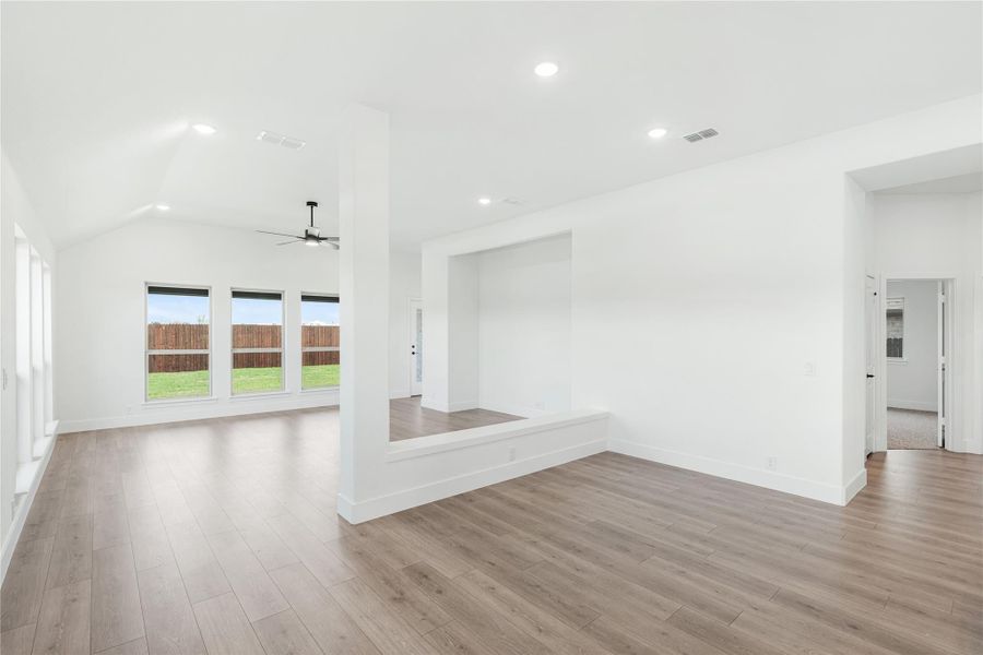 Open living area with vaulted ceiling, ceiling fan, hardwood floors, and large windows overlooking backyard