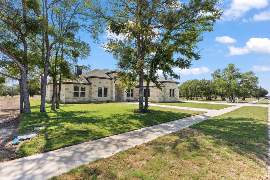 A striking stone facade home with an inviting front yard and concrete pathways, nestled among mature trees. A striking stone facade home with an inviting front yard and concrete pathways, nestled among mature trees.