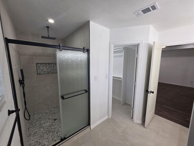 Full bathroom with a shower stall, a textured ceiling, and a walk in closet Full bathroom with a shower stall, a textured ceiling, and a walk in closet