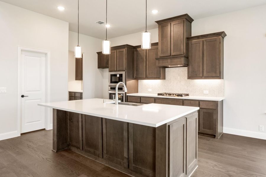 Kitchen with dark brown cabinets, large island with white countertop, pendant lights, and hardwood floors