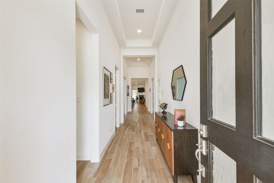 Wood and glass door opens to wood look tile entry with high trayed ceilings. Wood and glass door opens to wood look tile entry with high trayed ceilings.