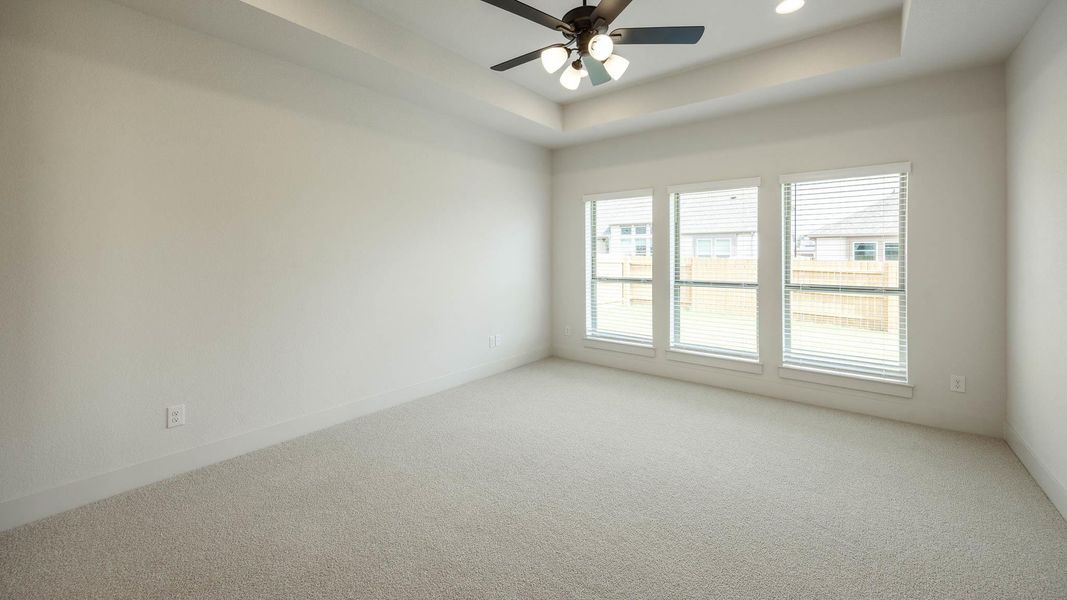 Carpeted spare room with a tray ceiling and ceiling fan