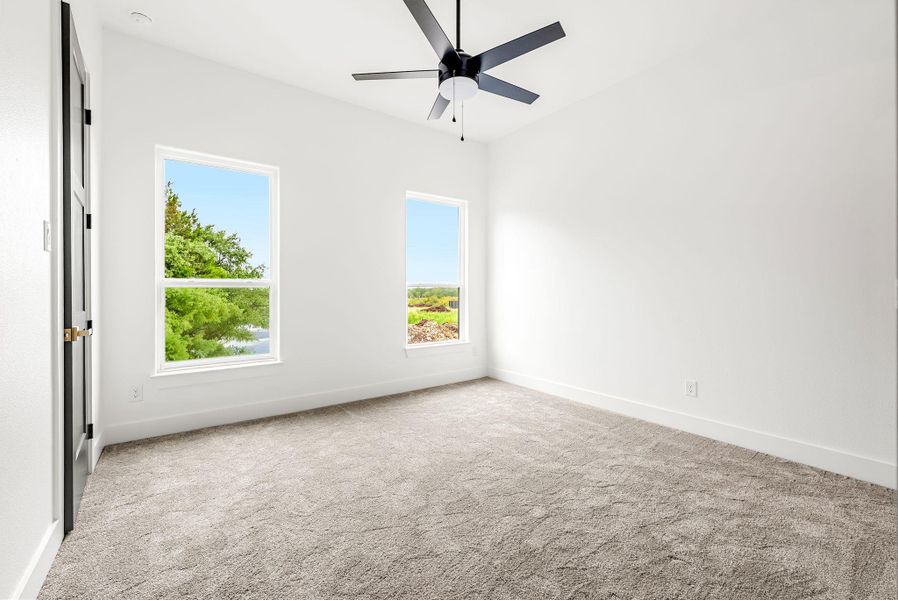 A quiet bedroom with ample natural light, soft carpeting, and a modern ceiling fan for comfort.
