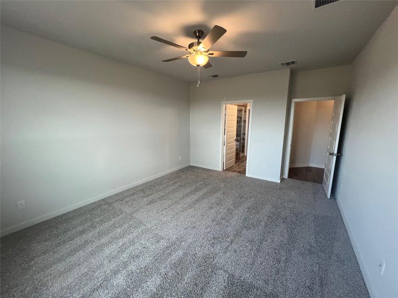 A spacious bedroom features plush carpeting and an overhead ceiling fan for comfort.