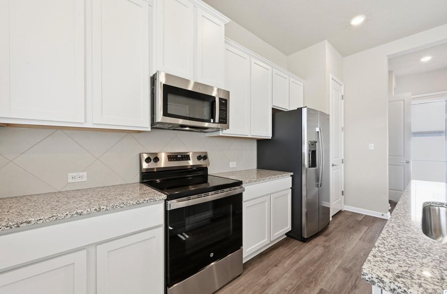 Kitchen featuring white shaker-style cabinetry, stainless steel appliances, speckled stone countertops, and a diagonally laid tile backsplash Kitchen featuring white shaker-style cabinetry, stainless steel appliances, speckled stone countertops, and a diagonally laid tile backsplash