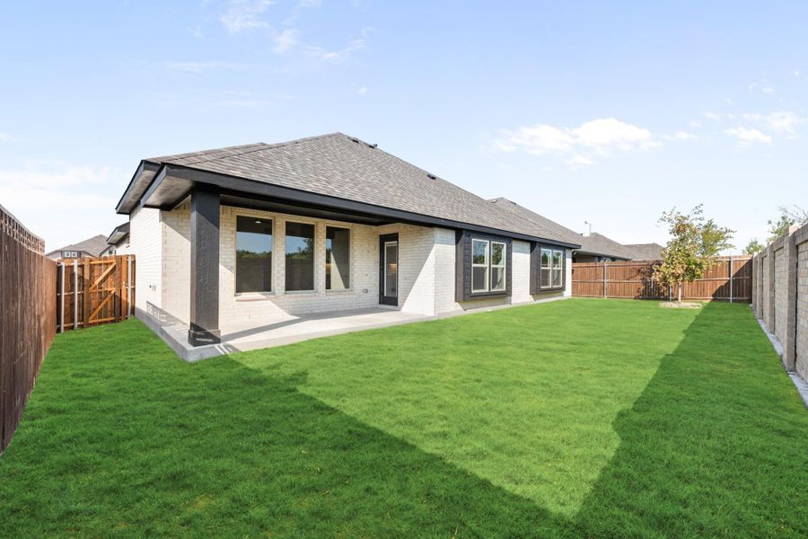 Rear view of single-story brick home with covered patio, large windows, and fenced backyard with green lawn Rear view of single-story brick home with covered patio, large windows, and fenced backyard with green lawn