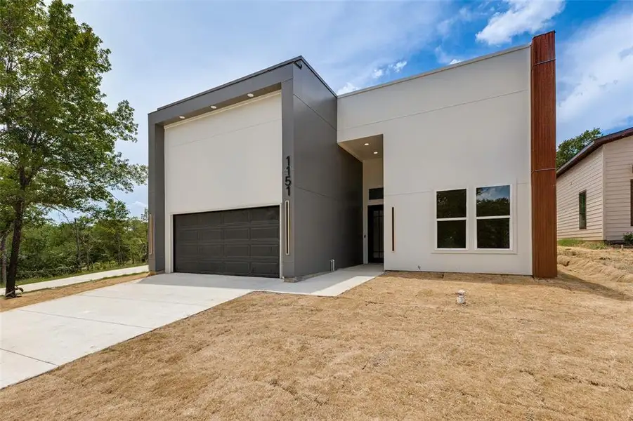 Modern facade featuring a gray paneled garage door, large numerical address display, and a prominent wood-finish architectural element Modern facade featuring a gray paneled garage door, large numerical address display, and a prominent wood-finish architectural element