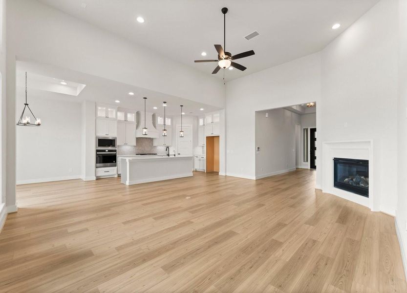 Spacious open-concept living area with 12 & 14"high ceilings and elegant wood flooring. Features a modern kitchen with a large island, pendant lighting, and built-in appliances. Includes a cozy fireplace, ceiling fan, and ample natural light, perfect for entertaining.