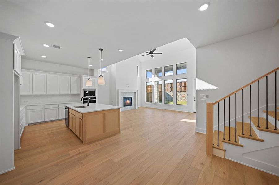 Kitchen featuring white cabinets, a kitchen island with sink, pendant lighting, open floor plan, and a glass covered fireplace