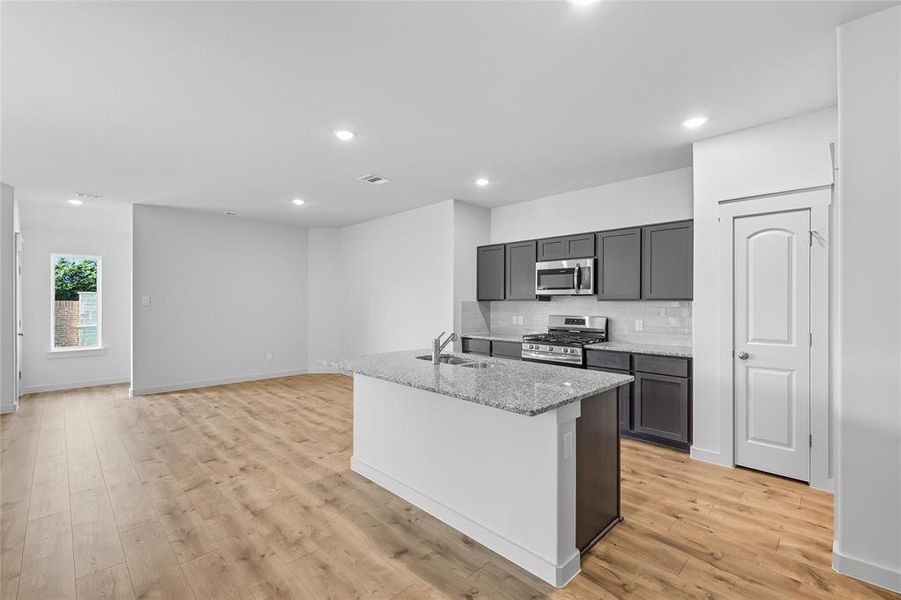Kitchen featuring tasteful backsplash, a kitchen island with sink, light stone counters, appliances with stainless steel finishes, and recessed lighting