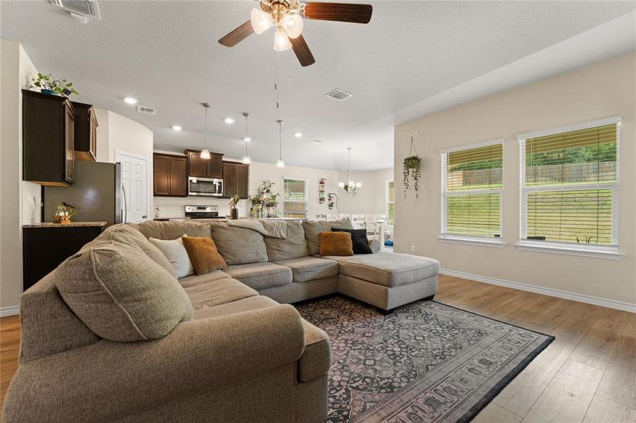 Living room with light wood-style flooring, a ceiling fan, a chandelier, and recessed lighting