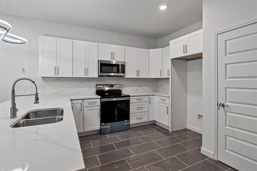 Kitchen with appliances with stainless steel finishes, decorative light fixtures, sink, white cabinets, and backsplash