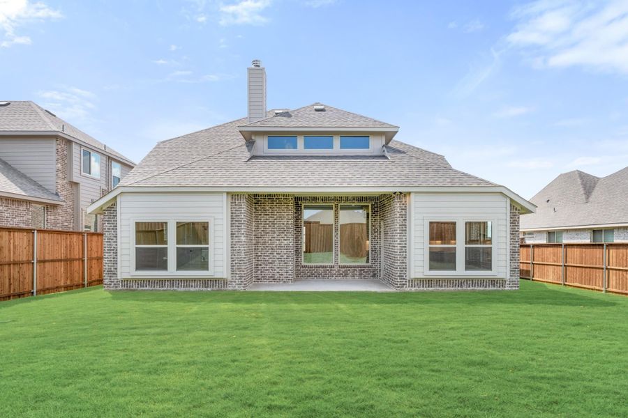 Rear exterior of single-story brick home with covered patio, chimney, and fenced backyard with green lawn