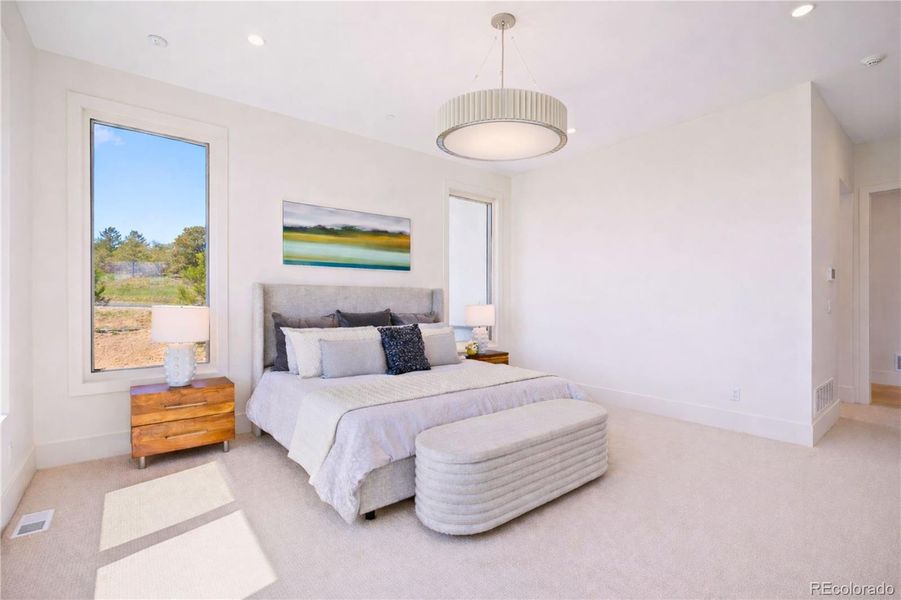 Bright primary bedroom with large picture windows, soft natural light, and a modern chandelier.