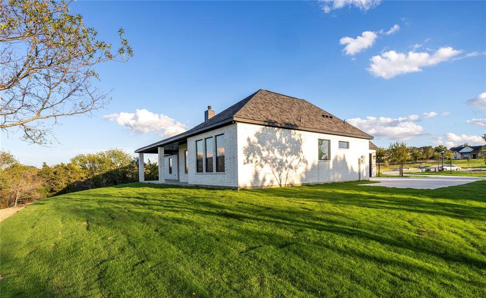 View of home's exterior featuring a lawn, brick siding, a chimney, a patio, and a shingled roof