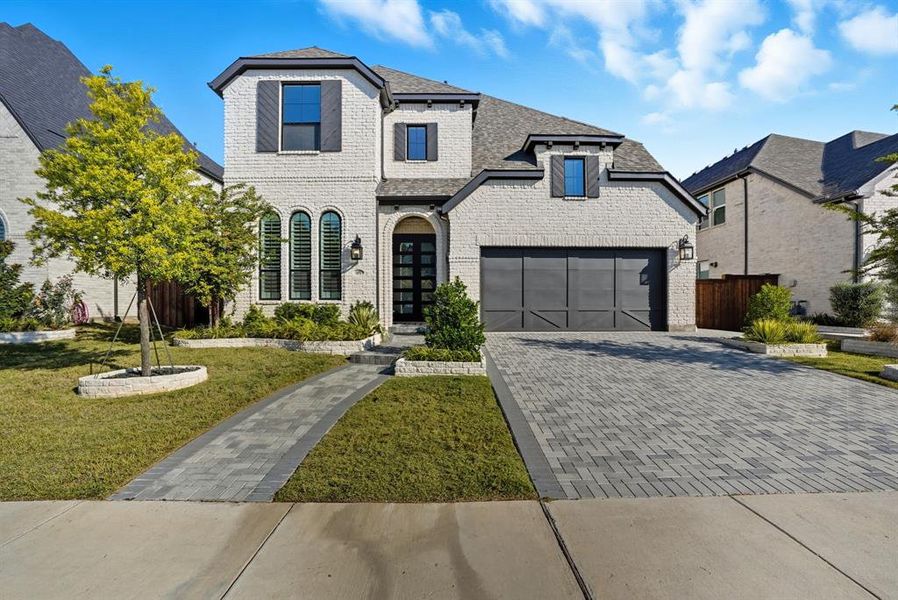 French country inspired facade featuring decorative driveway, brick siding, and a shingled roof French country inspired facade featuring decorative driveway, brick siding, and a shingled roof