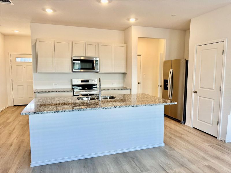 Kitchen featuring light stone counters, stainless steel appliances, and white cabinetry