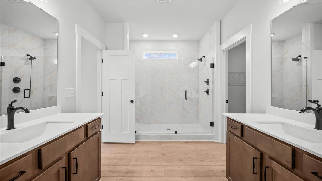 Dual vanities, timeless finishes, and a spa-inspired frameless tiled walk-in Roman shower create pure luxury