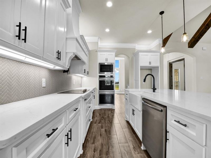 Kitchen with white cabinets, hanging light fixtures, appliances with stainless steel finishes, light stone counters, and dark wood-type flooring