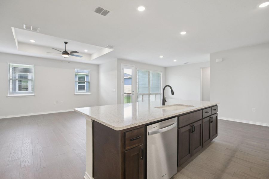 Kitchen with open floor plan, light wood finished floors, dark brown cabinetry, recessed lighting, and light stone countertops